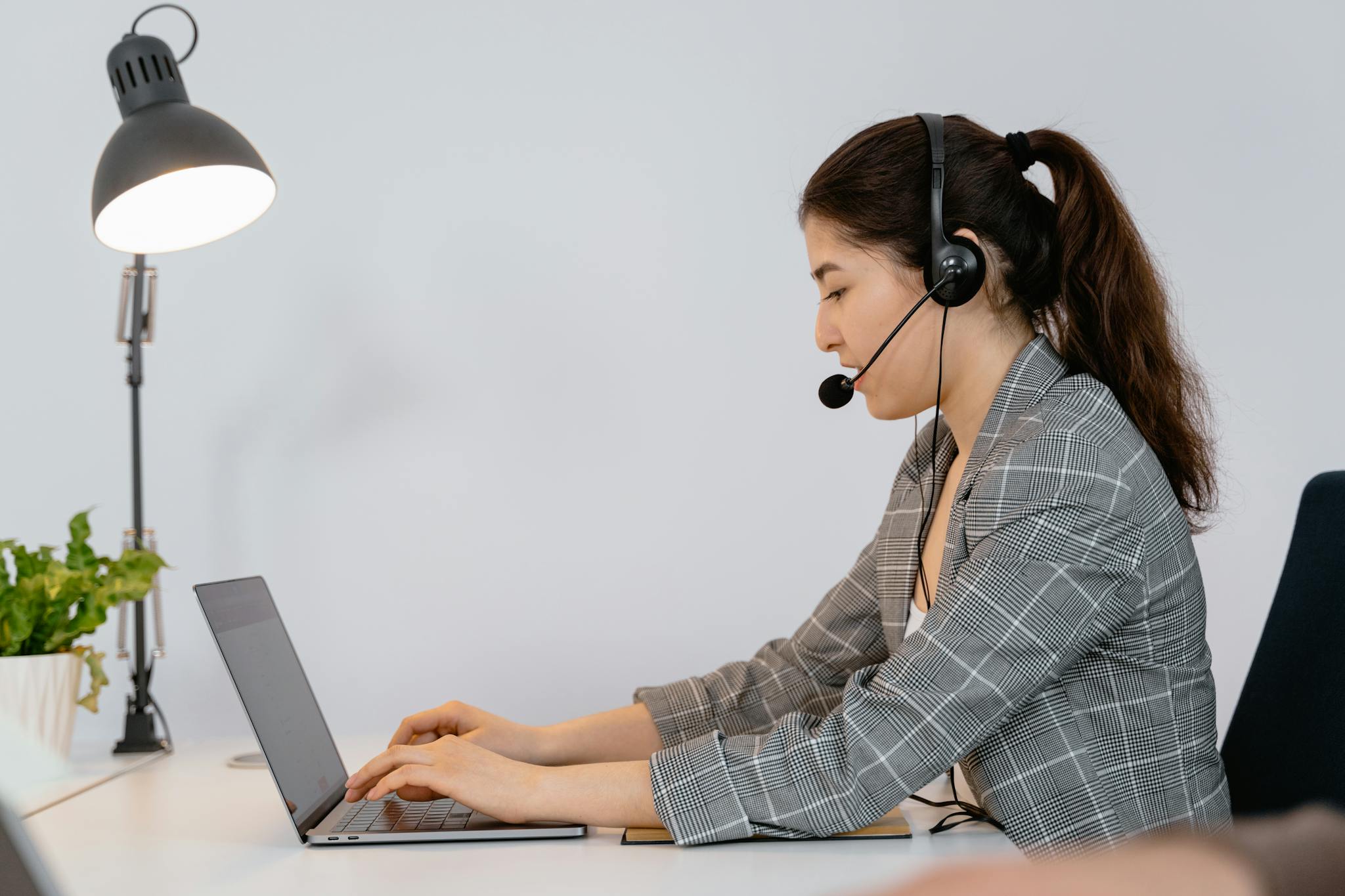 Professional woman in office with headset typing on laptop, offering customer support.